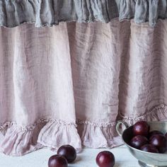 some plums are in a bowl next to a curtain with ruffle trim on it