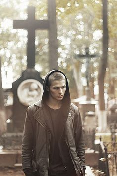 a young man wearing a hoodie and standing in front of a cross with his hands on his hips