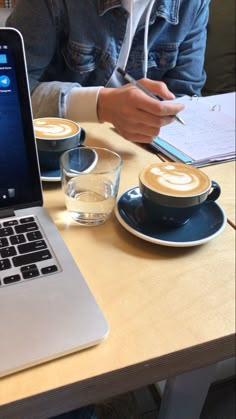 a laptop computer sitting on top of a wooden table next to two cups of coffee