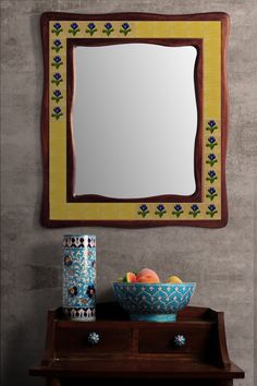 a bowl of fruit sitting on top of a wooden table next to a wall mirror