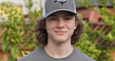 a young man with curly hair wearing a gray and white baseball cap is smiling at the camera