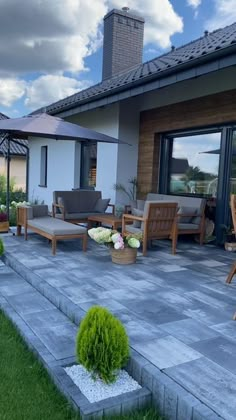 a patio with chairs, tables and umbrellas in front of a house on a cloudy day