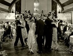 an old black and white photo of people dancing in a hall with tables full of people