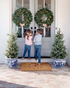 two young children standing in front of a door with wreaths on the doorsill