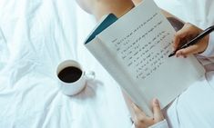 a person writing on a notebook with a cup of coffee