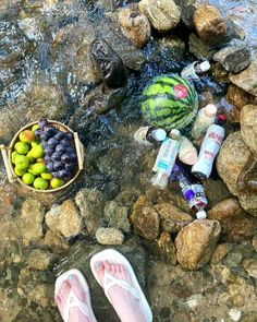 a person's feet in the water with fruit and watermelon on rocks