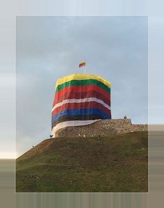 a large rainbow colored kite flying over a stone wall on top of a grassy hill