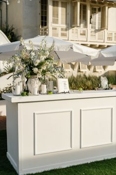 an outdoor bar with white umbrellas and flowers on the table in front of a building