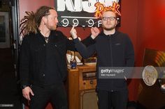 two men standing next to each other in front of a red wall with a neon sign