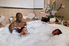 a man and two children in a bathtub with foam on the floor, surrounded by flowers