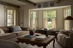 a living room filled with furniture and two large windows covered in sunlight shining through them