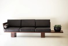 a black leather couch sitting on top of a wooden table next to a potted plant