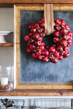 a wreath made out of apples hangs on a chalkboard