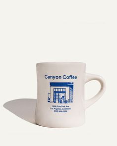 a white coffee mug with the canyon coffee logo on it's front and side