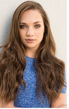 a woman with long brown hair and blue dress posing for a photo in front of a white wall