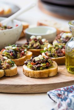 several pieces of bread with olives and other toppings on a cutting board next to bowls