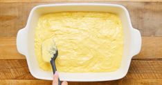 a person holding a spoon in a bowl of yellow batter on top of a wooden table