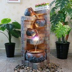 a water fountain in the middle of a room with potted plants and rocks around it