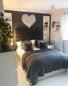 a black and white bedroom with a heart shaped wall hanging above the bed, along with potted plants