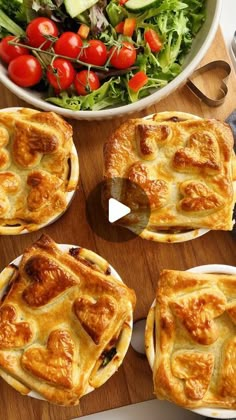 four pies on plates next to a bowl of salad and utensils in front of them