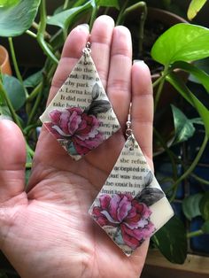 a pair of pink flowers are hanging from the back of a book page earring