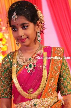 a woman in a pink and green saree with gold jewelry on her neck, smiling at the camera