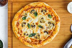 a pizza sitting on top of a wooden cutting board next to bowls of sauces