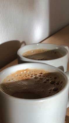 two white cups filled with liquid on top of a wooden table