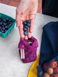 a person holding some blueberries in their hand next to a bag full of them