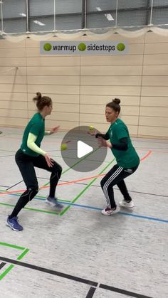 two women in green shirts are playing frisbee on an indoor basketball court with colored lines