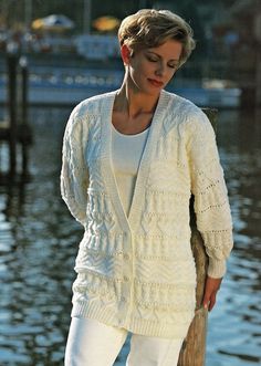 a woman in white is standing by the water wearing a cardigan sweater and pants