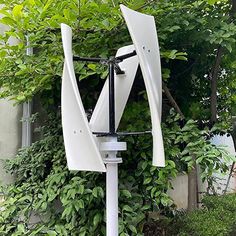 a white wind chime sitting on top of a metal pole next to a lush green bush