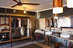 a bathroom with two sinks and a ceiling fan in the corner next to it is a closet full of hanging clothes