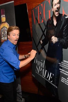 a man in blue shirt and black pants standing next to a poster with an image of david spade on it