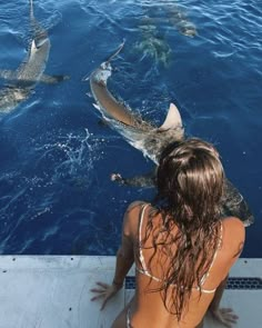 a woman sitting on the side of a boat looking at two sharks in the water