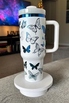 a white coffee cup with blue butterflies on it sitting on top of a table next to a tv