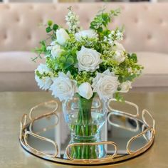 a glass vase with white flowers in it on a table next to a couch and coffee table