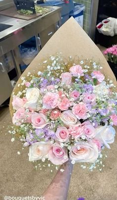 someone holding a bouquet of pink and white flowers in front of a counter top with other items on it