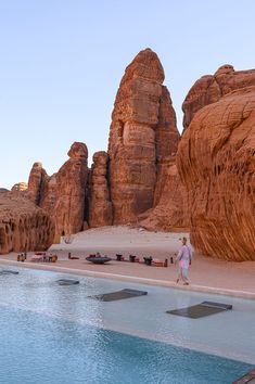 a person walking on the beach next to a pool in front of large rock formations