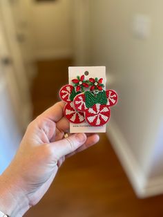 a hand holding up a christmas card with red and green decorations on it in front of a white wall