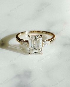 an emerald cut diamond engagement ring with baguets on the side and two bagsuetts at the top