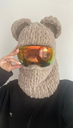 a person wearing a knitted bear mask with goggles on their face and one eye covered by a scarf