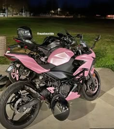 two pink motorcycles parked next to each other on the cement near some grass and trees