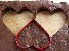 two heart shaped cookie cutters sitting on top of a piece of brownie with chocolate frosting