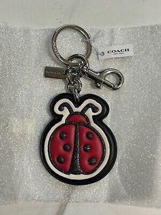 a red and black lady bug keychain on a white cloth with the name coach