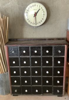 a clock mounted to the side of a wall next to a black cabinet with drawers