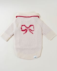 a white sweater with a red bow on the front and back, sitting on top of a table