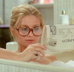 a woman wearing glasses is sitting in a bathtub and looking at the soap on her hand