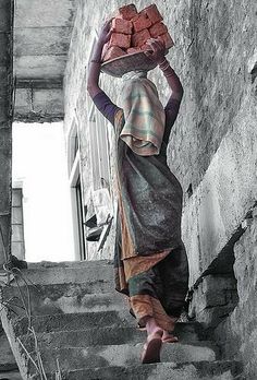 a woman walking up some stairs carrying bricks on her head