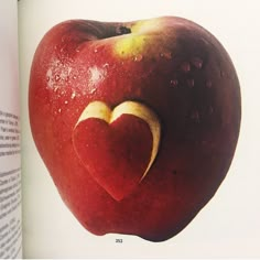 an apple with a heart cut out of it's side in front of a book